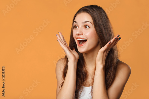 Surprised happy beautiful woman looking sideways in excitement. Isolated on orange background