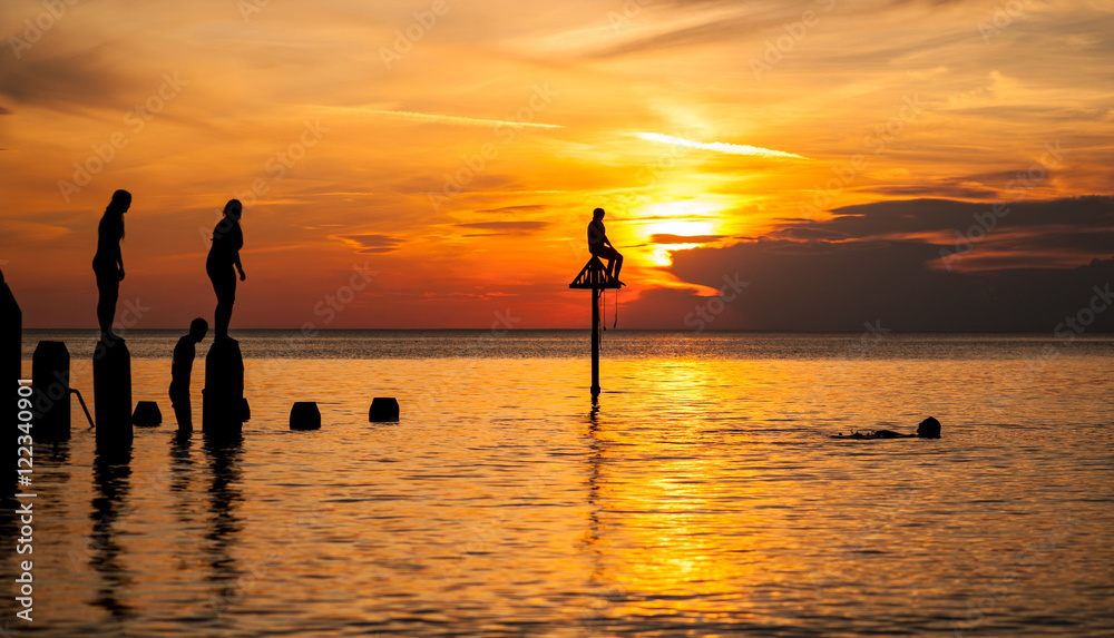 People enjoying a swim and diving from a jetty at sunset.