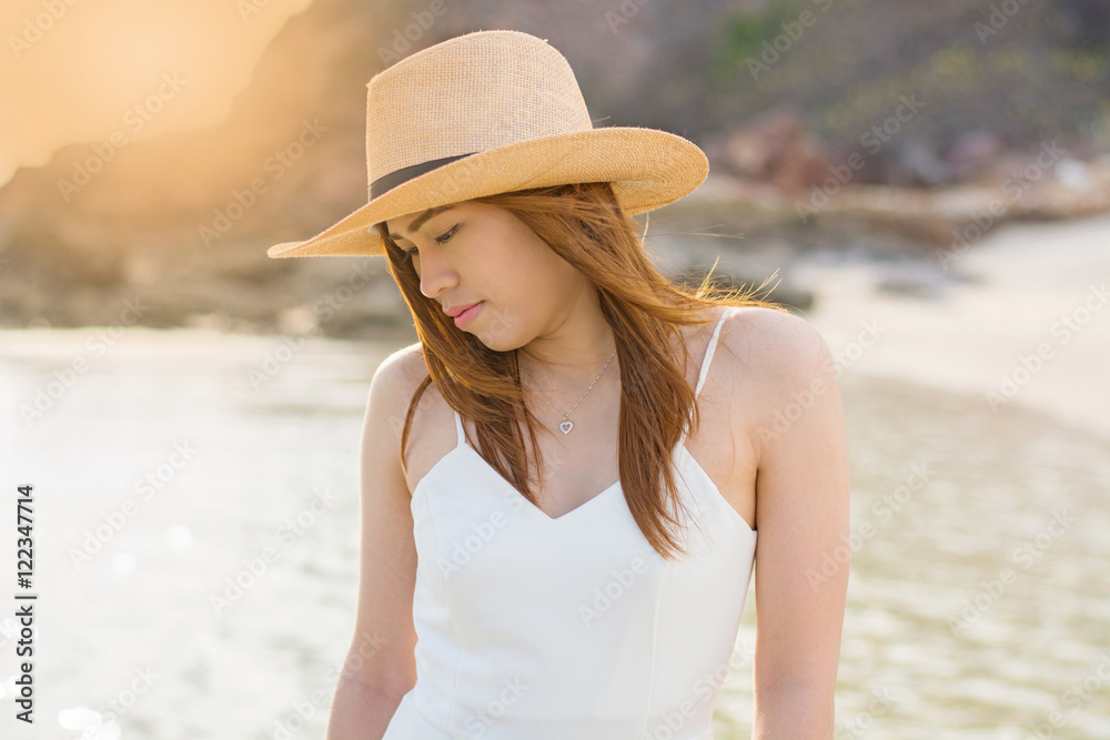 Young woman in long white dress and hat leying on white sand  at sunset on the sea. having great summer time on holidays. Summer vacation, holidays, serenity, travel,
