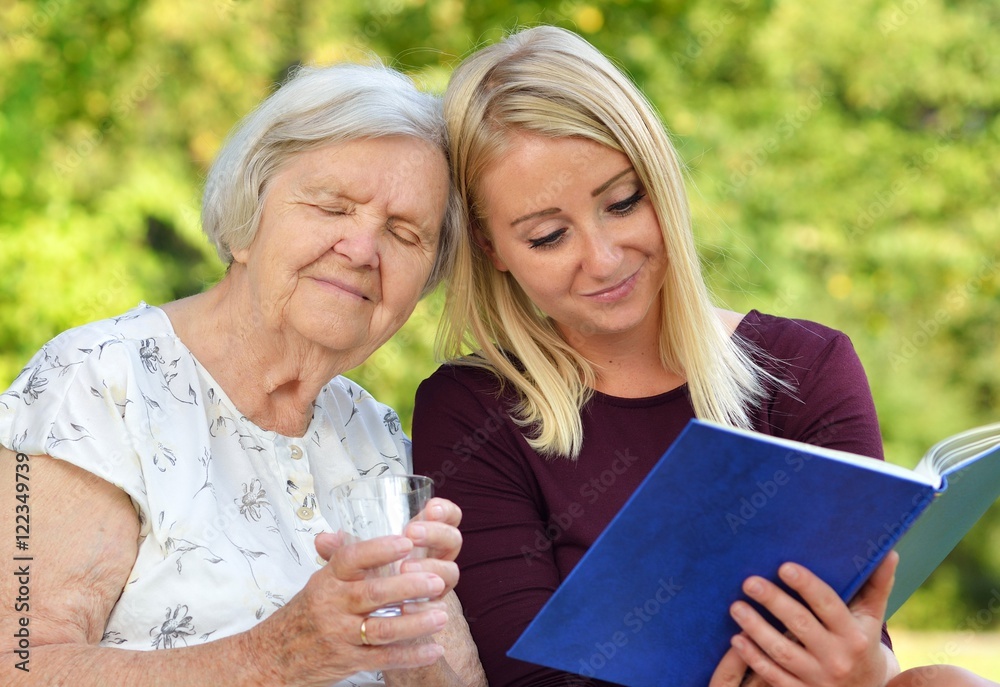 Young woman reading a book elderly woman in the park.