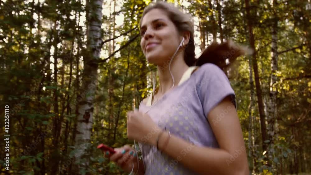 Attractive smiling woman runs around the park that is full of green trees Attractive smiling woman runs around the park that is full of green trees