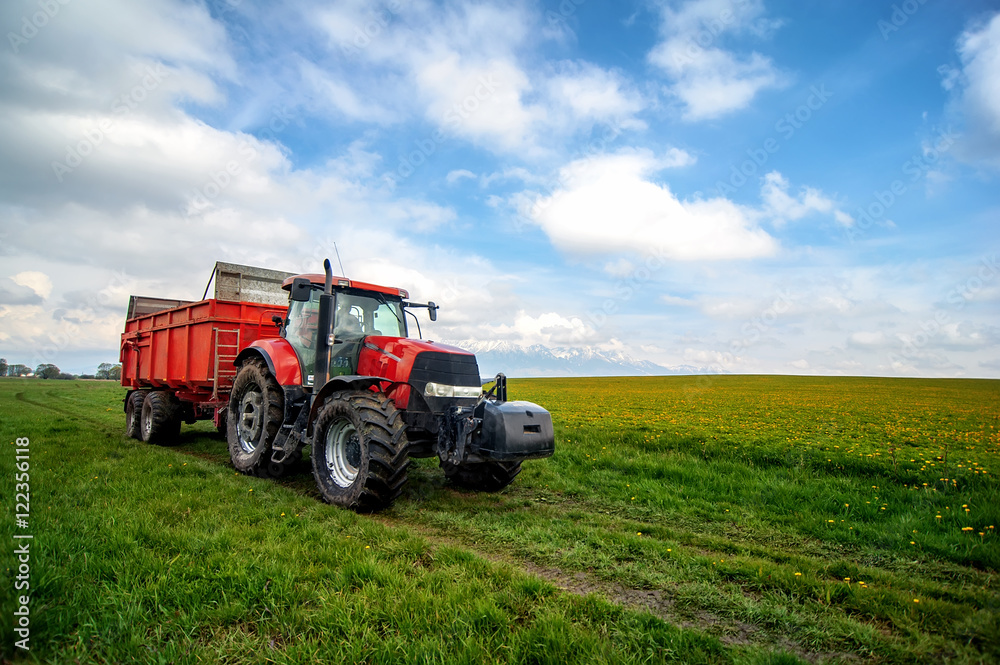 huge tractor in floral spring field under the blue cloudy sky huge tractor in floral spring field under the blue cloudy sky