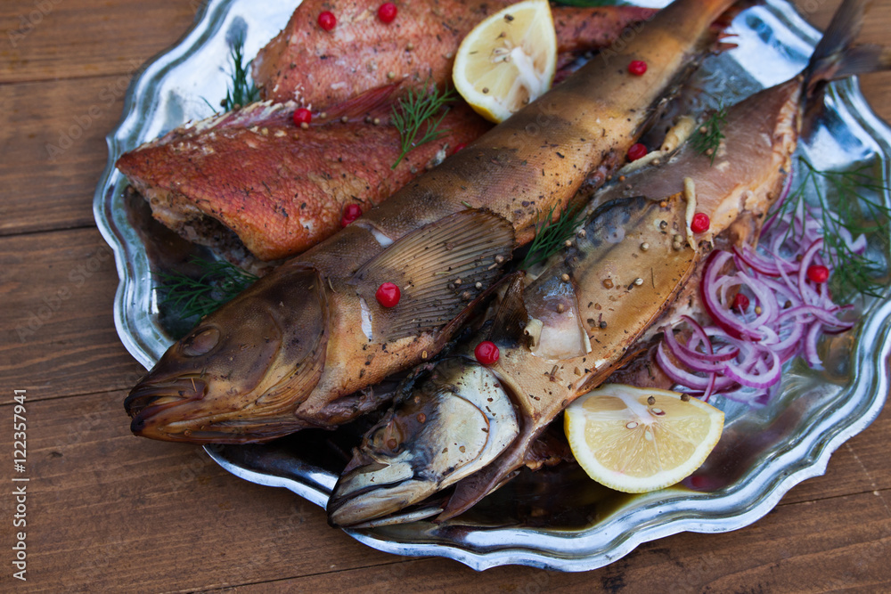 smoked fish mackerel, sea bass and lingcod on metal plate, wooden background smoked fish mackerel, sea bass and lingcod on metal plate, wooden background