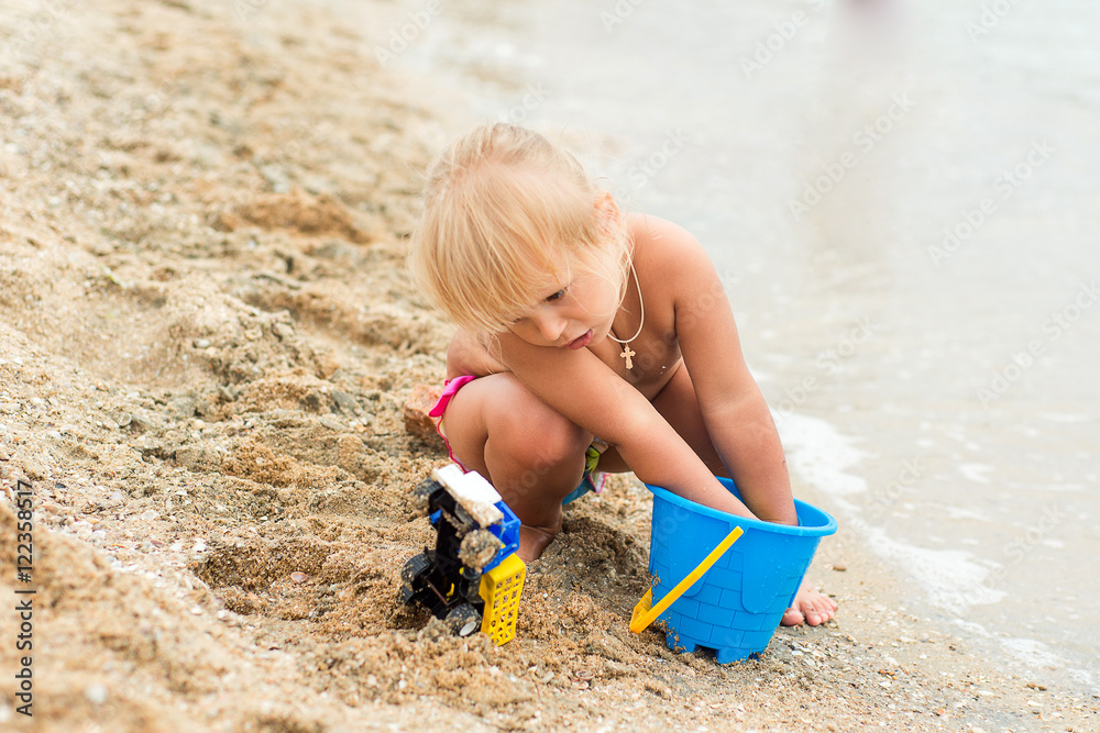 Adorable toddler girl playing with beach toys on white sand beach Adorable toddler girl playing with beach toys on white sand beach