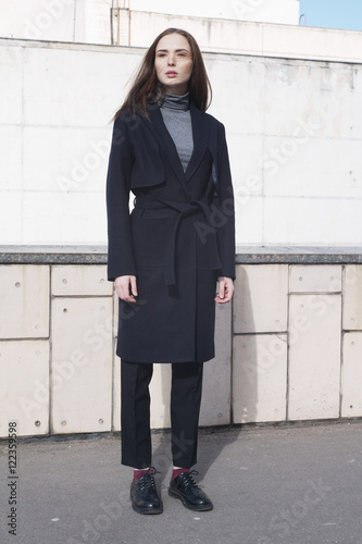 young female fashion model in classic navy trench coat, melange blouse and black boots - street style photo