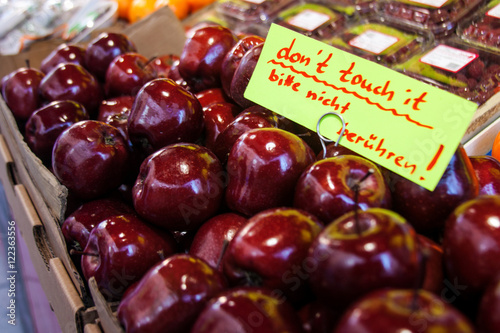 Lots of red-ripe apples in the portable stall at the market in Austria with a hadwritten caution board "Don't touch".