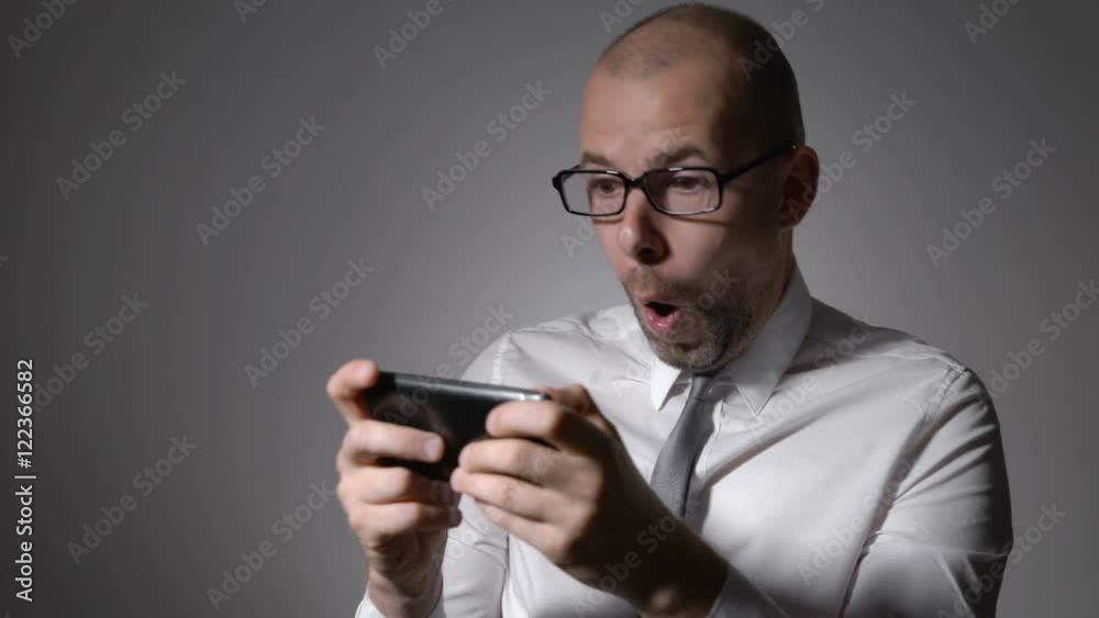 Very expressive and emotional Manager in white shirt and tie playing games on his smartphone. Very expressive and emotional Manager in white shirt and tie playing games on his smartphone.