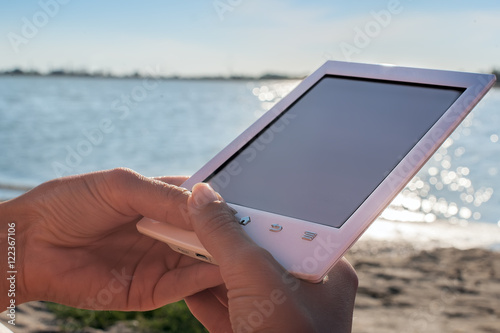 wooman sitting on sandy beach and holding bookreader photo