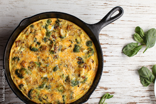 Baked egg frittata with spinach, cheese, broccoli, red potatoes, bacon, milk, and spinach top view photo