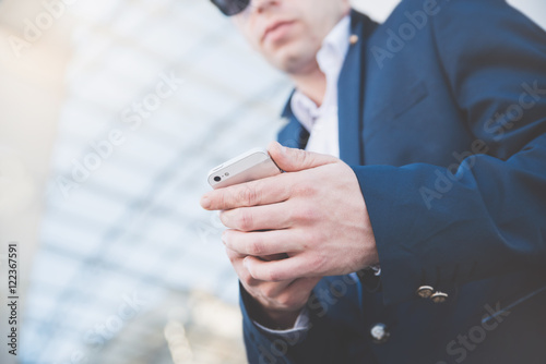Businessman with telephone in hand and holding a newspaper. Stylish man at the railway station in a blue jacket.