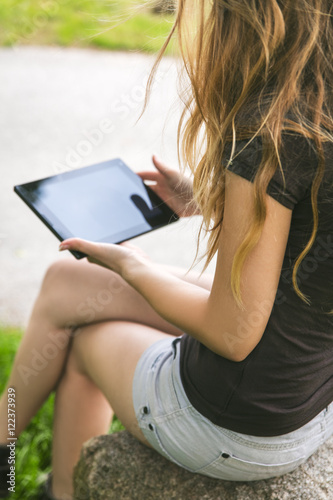 Junge Frau sitzt mit Tablet an der Straße photo