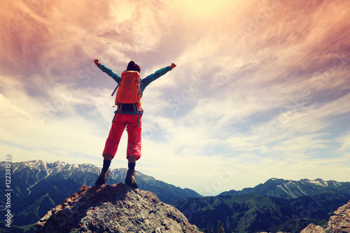 cheering young woman hiker open arms on mountain top.. photo