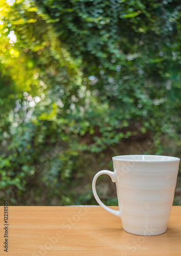 a selective focus picture of a cup of coffee on wooden table in green garden	