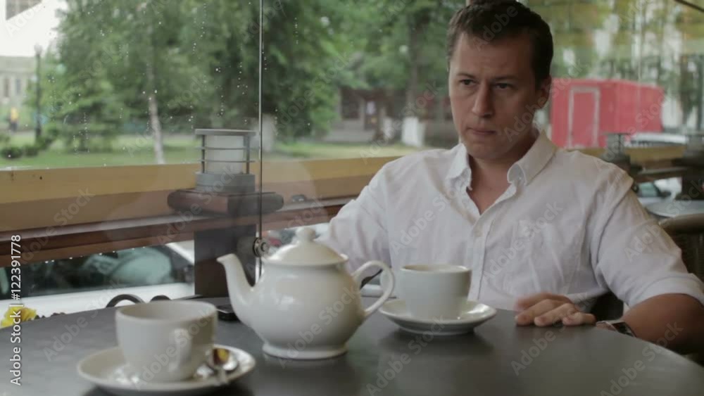 The man is nervous and looks at the clock waiting for the meeting sitting in a summer cafe. The man is nervous and looks at the clock waiting for the meeting sitting in a summer cafe.