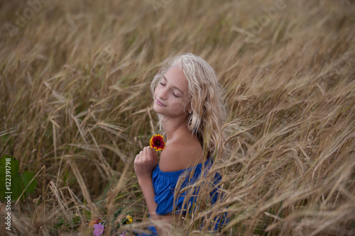 The girl in the blue dress in a field with bouquet of flowers