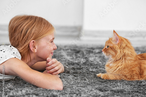 Beautiful little girl lying on floor with red fluffy cat