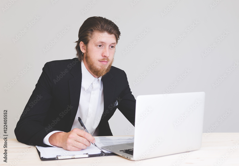 portrait of young male business man taking notes on paper while working with computer at office . portrait of young male business man taking notes on paper while working with computer at office .