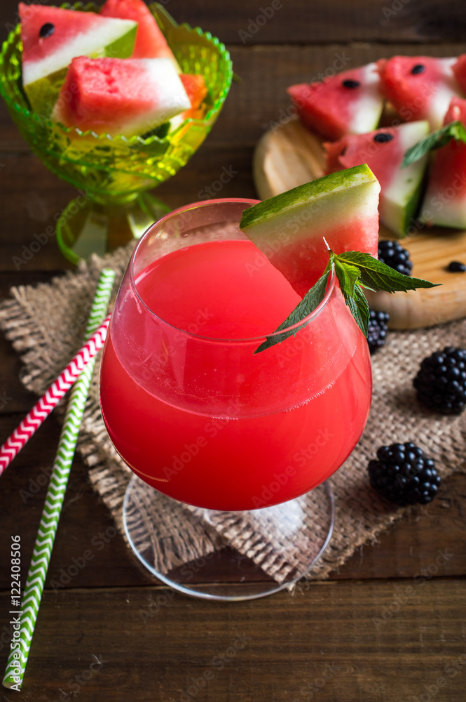 fresh watermelon in a glass with straws on a napkin. Triangular pieces of watermelon with mint and blackberries on a wooden board and a bowl. On a wooden background. fresh watermelon in a glass with straws on a napkin. Triangular pieces of watermelon with mint and blackberries on a wooden board and a bowl. On a wooden background.