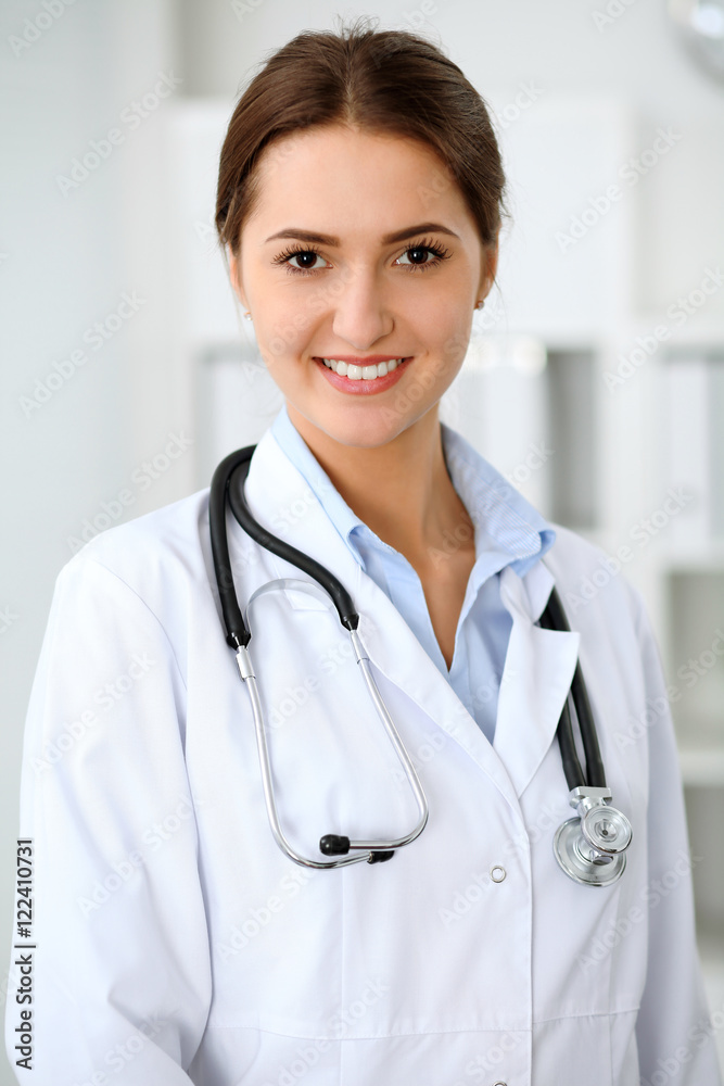 Young brunette female doctor standing with clipboard and smiling at hospital. Physician ready to examine patient Young brunette female doctor standing with clipboard and smiling at hospital. Physician ready to examine patient