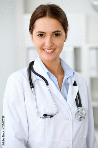Young brunette female doctor standing with clipboard and smiling at hospital.  Physician ready to examine patient