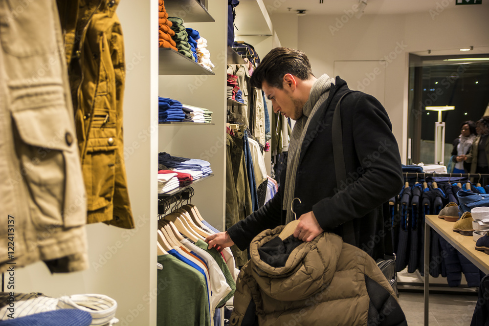 Side view of young male customer choosing shirt in menswear shop Side view of young male customer choosing shirt in menswear shop