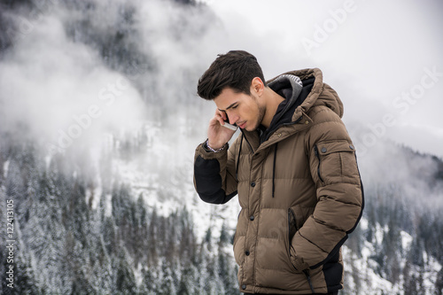 Canvas Print Dark haired handsome young man in winter outerwear using cell phone or smartphon