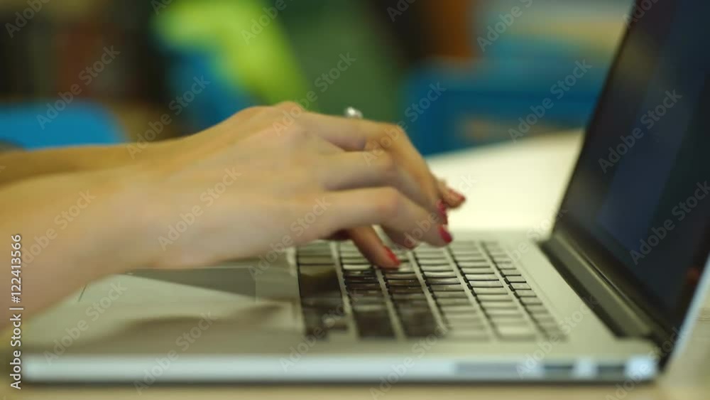 Close-up of female hands typing text message on laptop indoors, young female student sitting on the library stairs and using portable computer Close-up of female hands typing text message on laptop indoors, young female student sitting on the library stairs and using portable computer