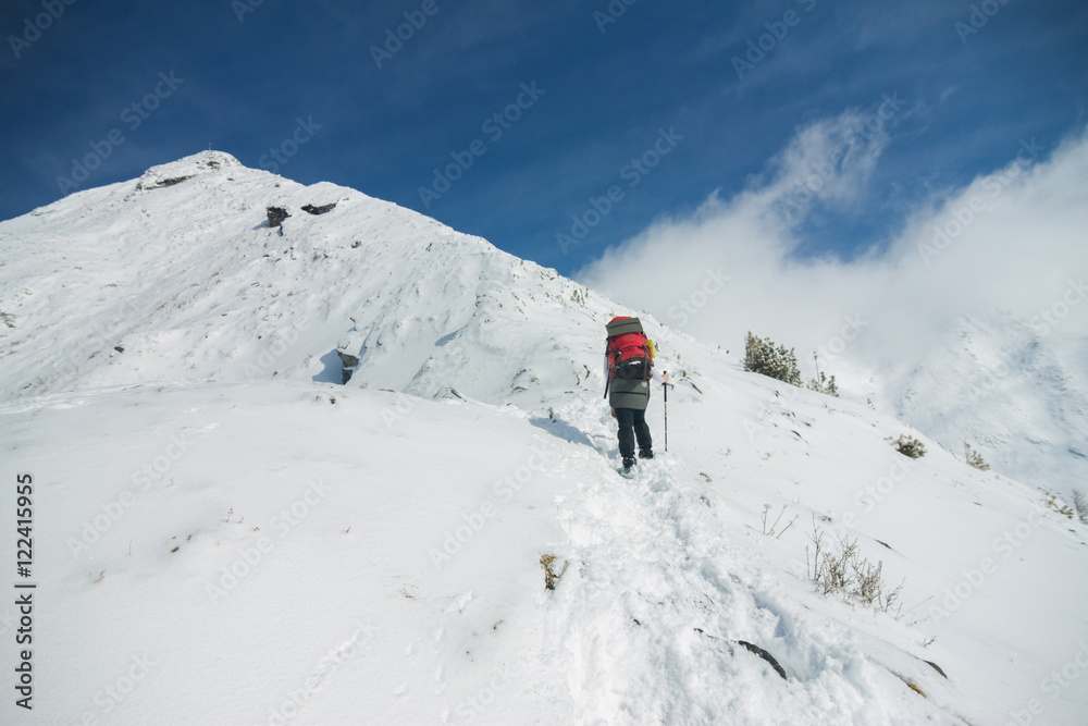 Woman tourist with a backpack climbs in snowy mountain