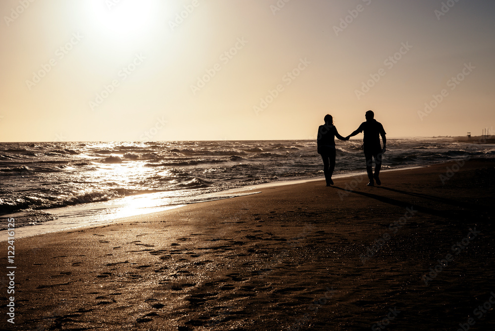 Couple walking on the beach at sunset.