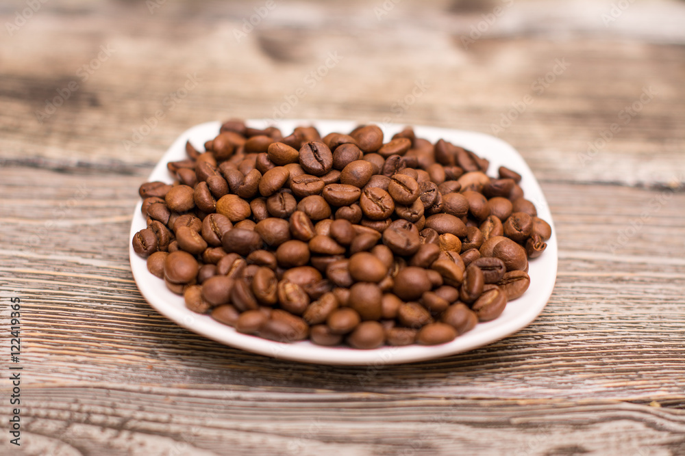small white saucer with cocoa beans on wooden background