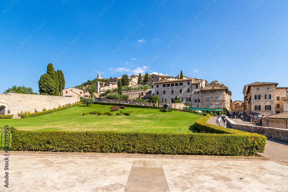 Assisi, Italy. The city view with the lawn in front of St. Francis Cathedral: Tau cross and motto of the Franciscan «Pax et Bonum»