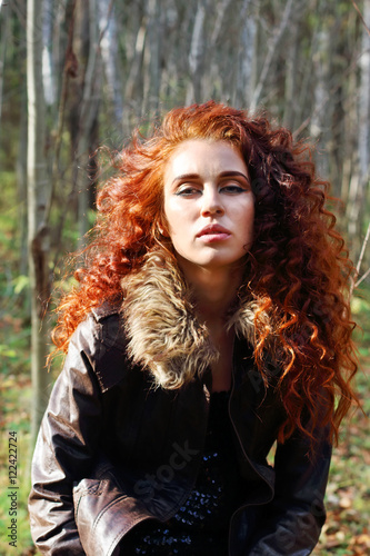 Beautiful woman in leather jacket poses in sunny autumn forest