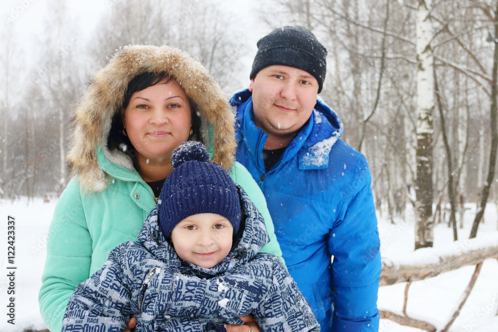 Happy family (mother, father, son) pose during snowfall in winte