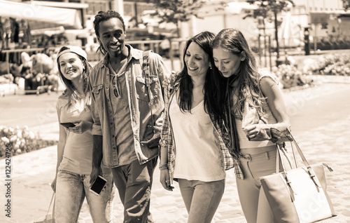 Cheerful friends walking in city center with phones and bags in their hands 