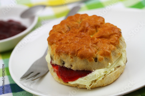 Freshly baked English scone with traditional clotted cream and strawberry jam on white plate 