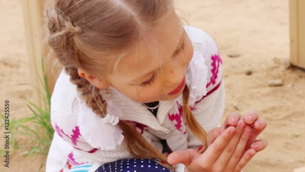 Happy gilr plays with bright ladybug sitting on finger outdoor, closeup