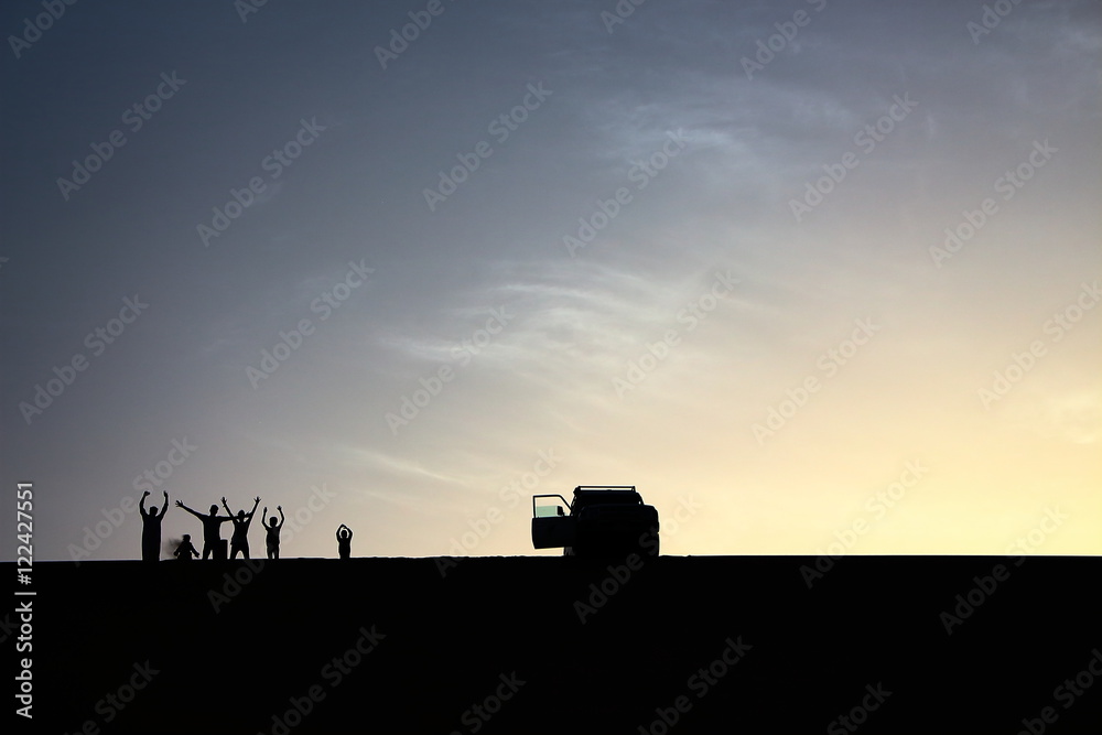 Fototapeta premium A pack of adventurers salute from the top of a grand sand dune while enjoying a beautiful summer sunset in Dakhla Oasis, Egypt.
