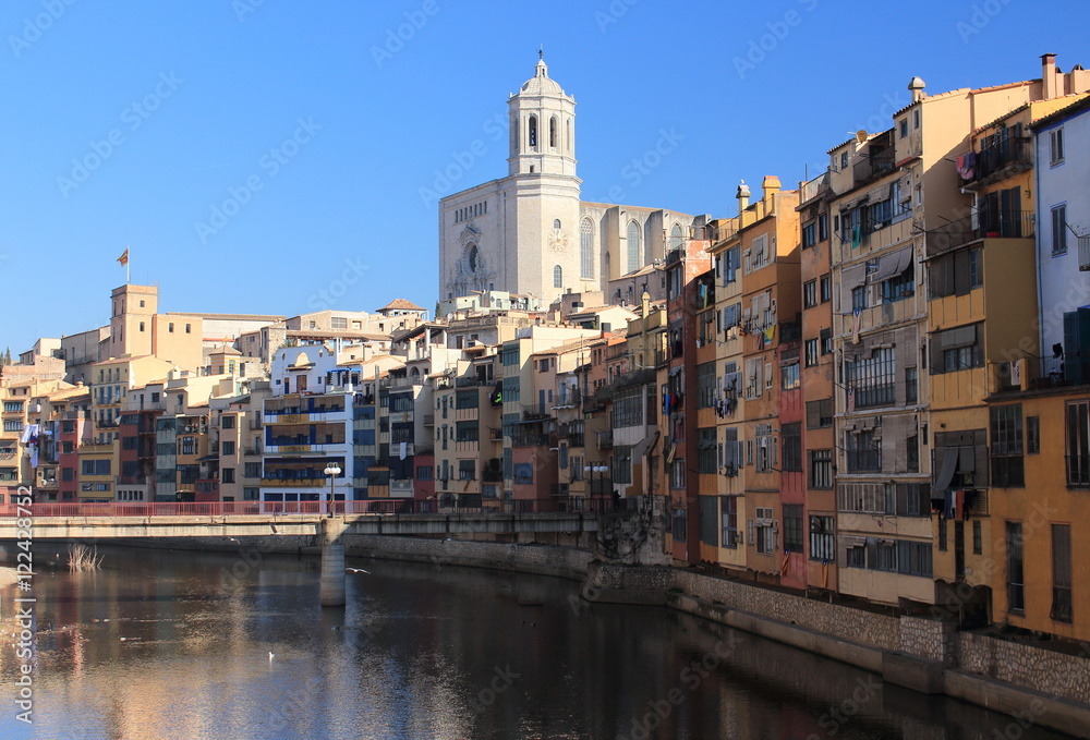 Colorful houses placed close to the Onyar River with amazing cathedral's main tower on backwards, Girona, Spain. 