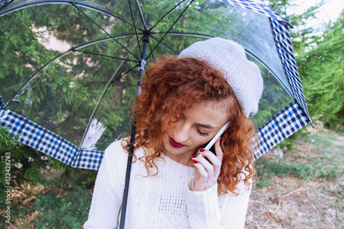 Mujer joven bajo un paraguas hablando por teléfono con gesto triste photo