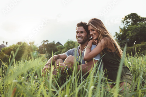 Young happy lovers sitting on meadow