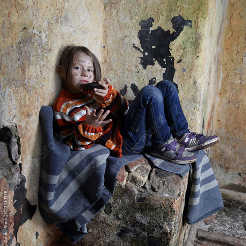 with dirty face sits on old blanket in basement and eats rough black bread - refugee orphan, hunger concept