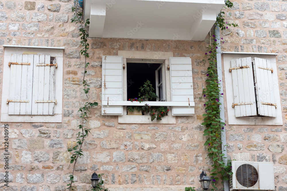Open Window with flowers and two closed windows with white shutters on a stone wall Open Window with flowers and two closed windows with white shutters on a stone wall