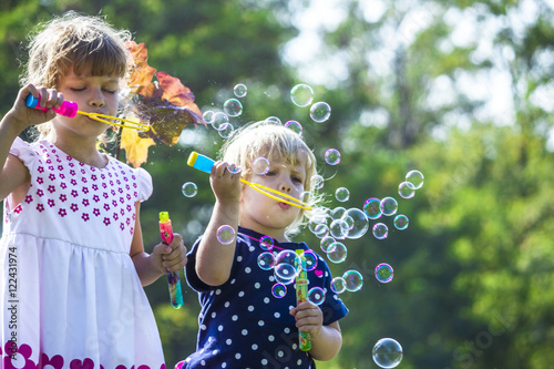Two funny little sisters blowing soap bubbles outdoors