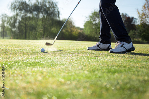 Golfer hitting iron club on golf course on fairway.