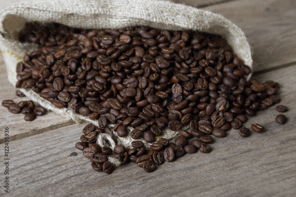 Fototapeta premium Coffee beans spread out from sackcloth sack to rough wooden table