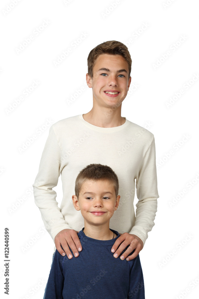 Teenage boys stands behind putting hands on his little brother shoulders isolated on white background - focus on little boy face