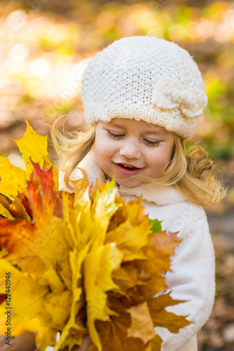 Joyful little girl in park in autumn with leaves in their hands