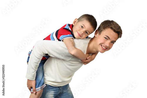 Older boy carries little brother on back isolated on white background