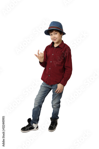 Teenage boy in blue hat, red shirt, jeans and sneakers shows horns (hard rock) gesture full height isolated on white background