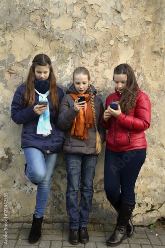 Internet and social networks replace live communication. Three girls together chat using their smartphones outdoor - vertical